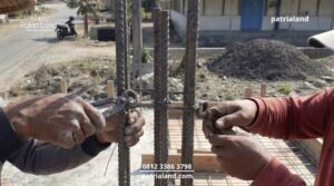 Tukang bangunan profesional sedang memastikan panjang overlap sambungan besi kolom lantai dua sejajar dan mengikatnya dengan kuat sebelum dicor.