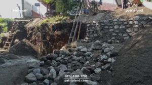 Persiapan material material berkualitas tinggi seperti batu kali dan pasir untuk pembuatan struktur penahan tanah di lahan berkontur miring.