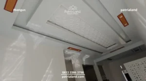 Interior mewah dengan plafon PVC drop ceiling motif 3D dan aksen kayu, ditambah pantulan cahaya alami dari desain roster.