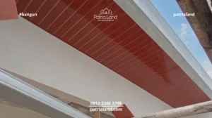 Proses pemasangan plafon PVC motif kayu warna merah kecokelatan menggunakan rangka hollow oleh pekerja konstruksi profesional.
