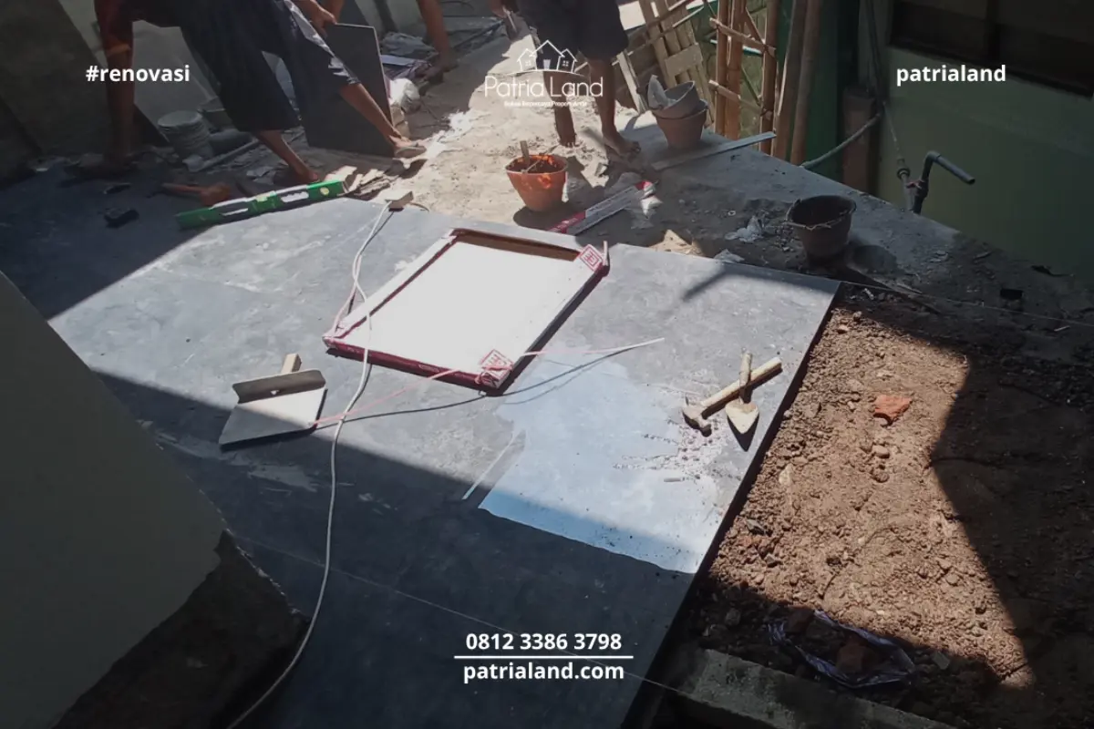 Pekerja profesional PatriaLand melakukan instalasi lantai keramik gelap yang presisi pada area teras Wisma Mubaligh.